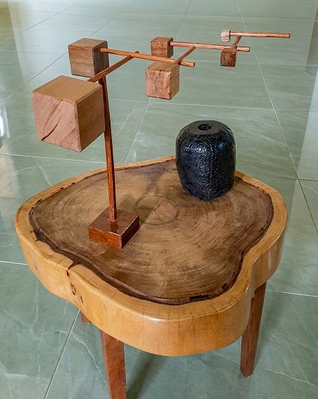 Móbile Equilibrium em madeira, com cubos suspensos, sobre mesa de tronco maciço