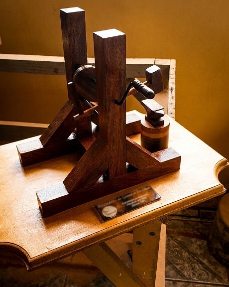 Escultura cinética em madeira escura com mecanismo de martelo e bigorna